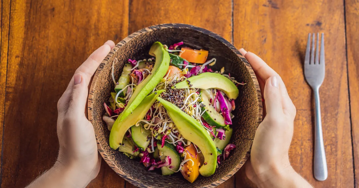 Bol de quinoa con salmón, pepino y aguacate sobre una mesa de madera con luz natural