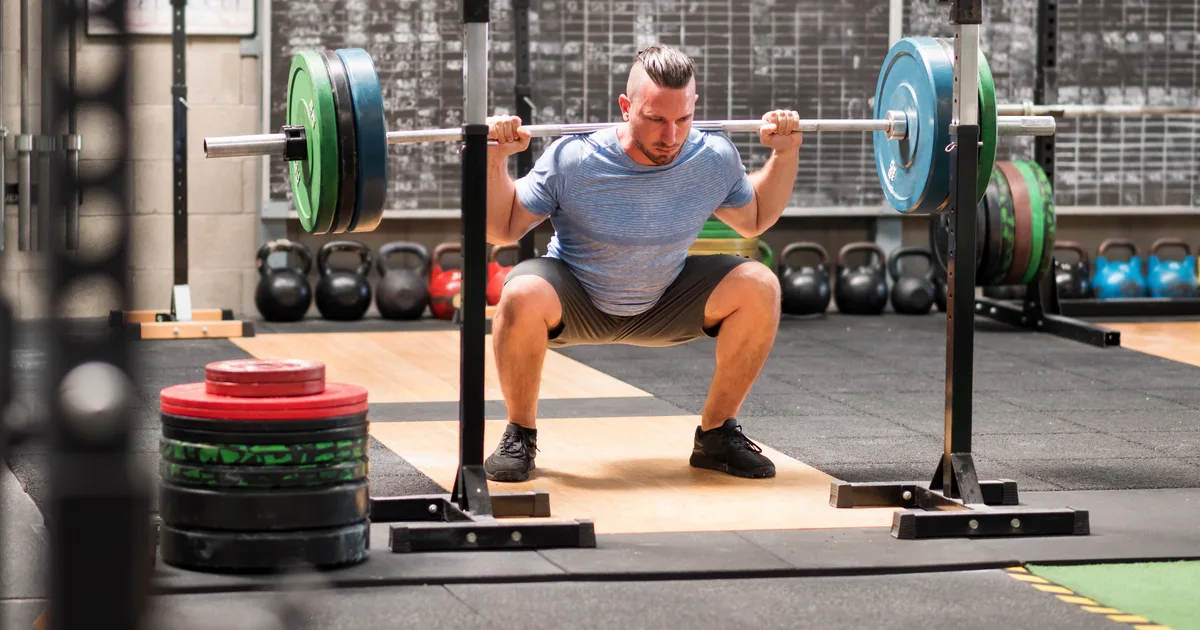 Deportista haciendo una sentadilla con barra en el gimnasio, de perfil, con buena postura de espalda