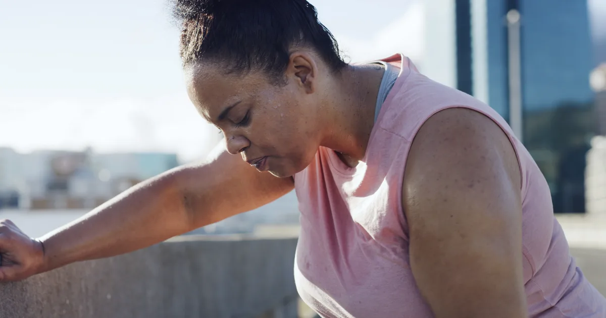 Mujer con ropa deportiva sentada y agotada tras entrenar al aire libre