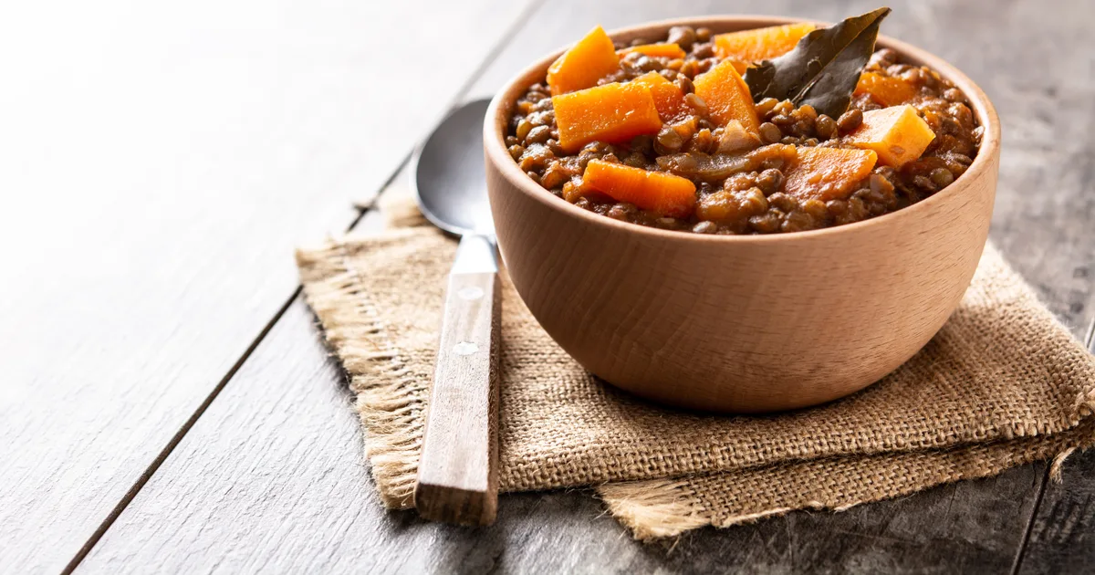 Cuenco de madera con guiso de lentejas con calabaza y zanahoria sobre una mesa de madera